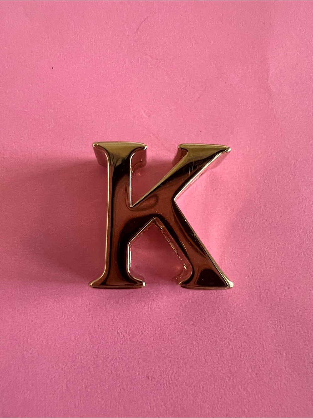 Dior Gold 'K' Letter Charm on Pink Background